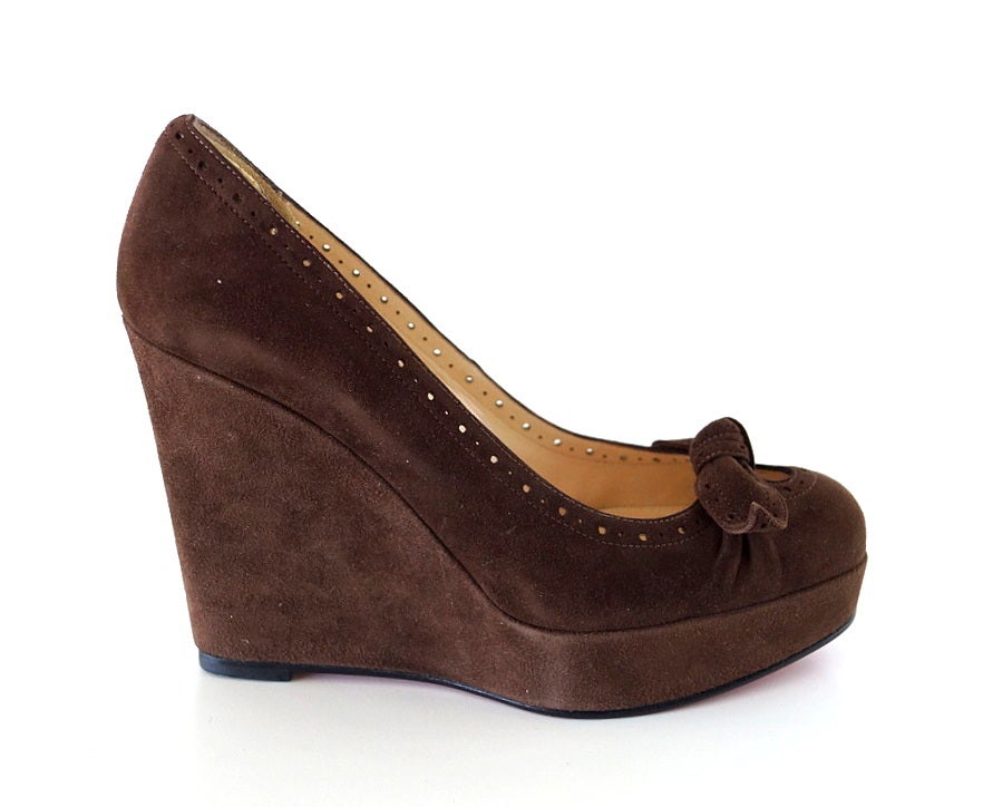 Guaranteed authentic Christian Louboutin fabulous chocolate brown suede wedge pump.  
Gorgeous cut on the foot.
Rounded toe.
Edged in wingtip style  perforation.
Top of the foot has a small bow and an opening.
NEW or NEVER WORN.
Signature red