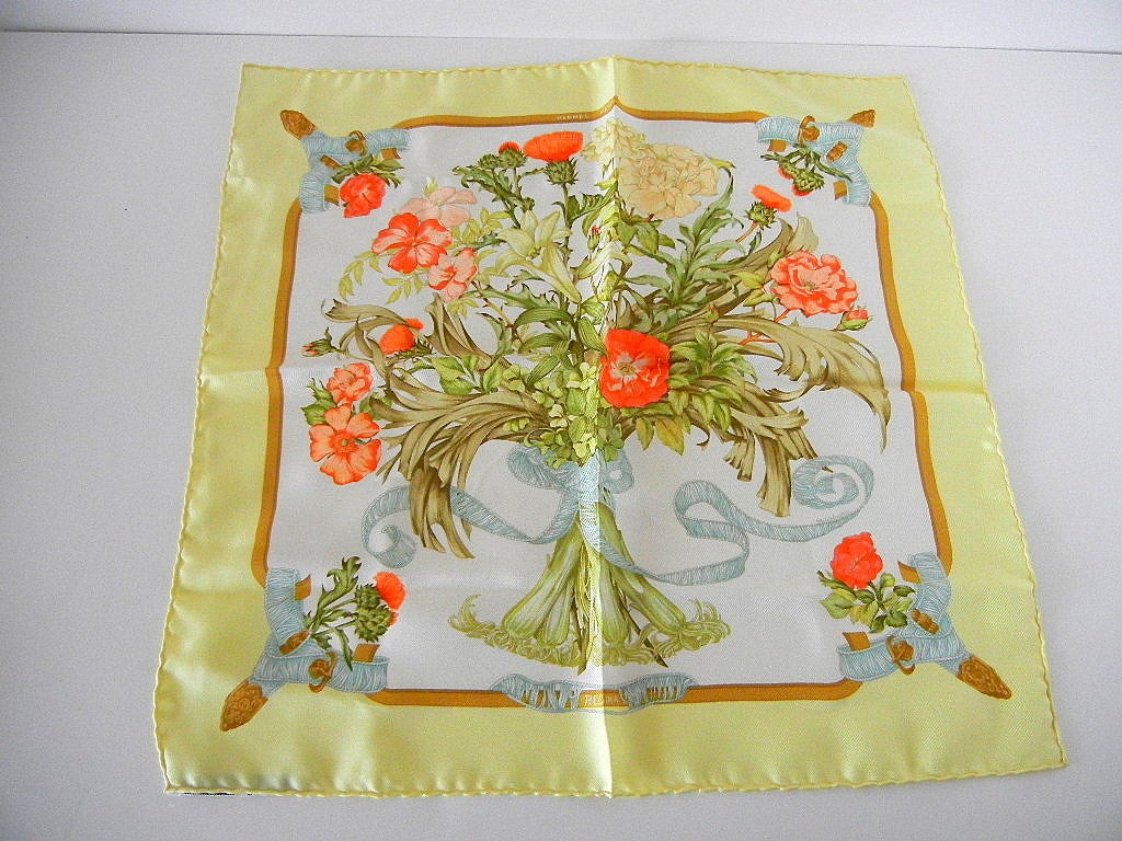 A bouquet of flowers and leaves in shades of greens, yellow, and oranges tied together with a soft aqua coloured cord. 
The background is a soft buttery yellow. 
Set 1 1/2