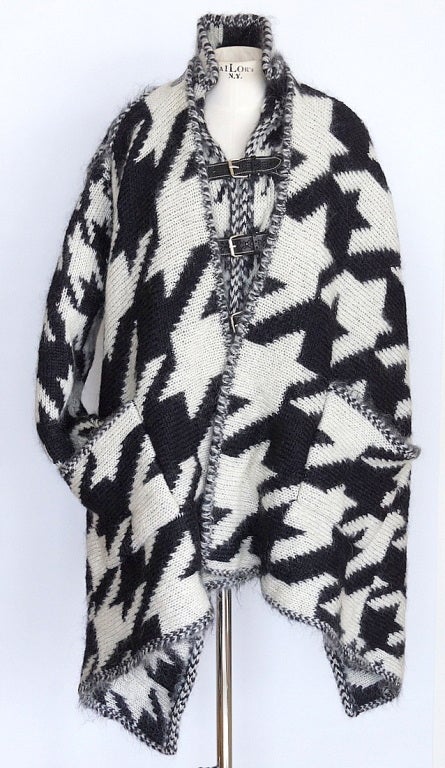 Alexander McQueen black and white cardigan in chunky Houndstooth mohair blend.
Raised seams, high neck, full sleeves, two front patch pockets, asymmetric hem.
Black perforated leather and silver-tone buckle fastenings at front and rear of