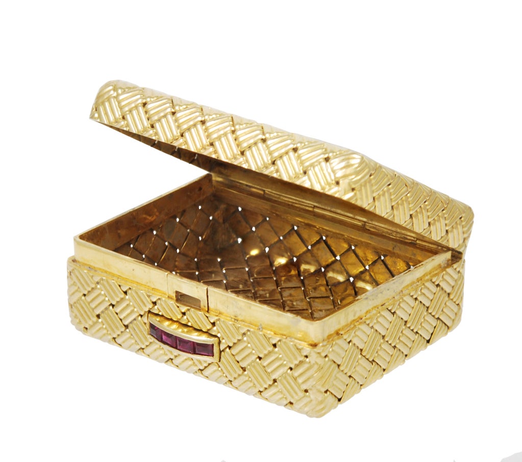 Elegant 18K gold hinged pill box, made and signed by Tiffany & Co. Woven texture. Clasp set with fine calibre-cut rubies. This box is beautiful to hold. It is solid and rectangular in shape, with softly rounded corners. Deep enough to hold most