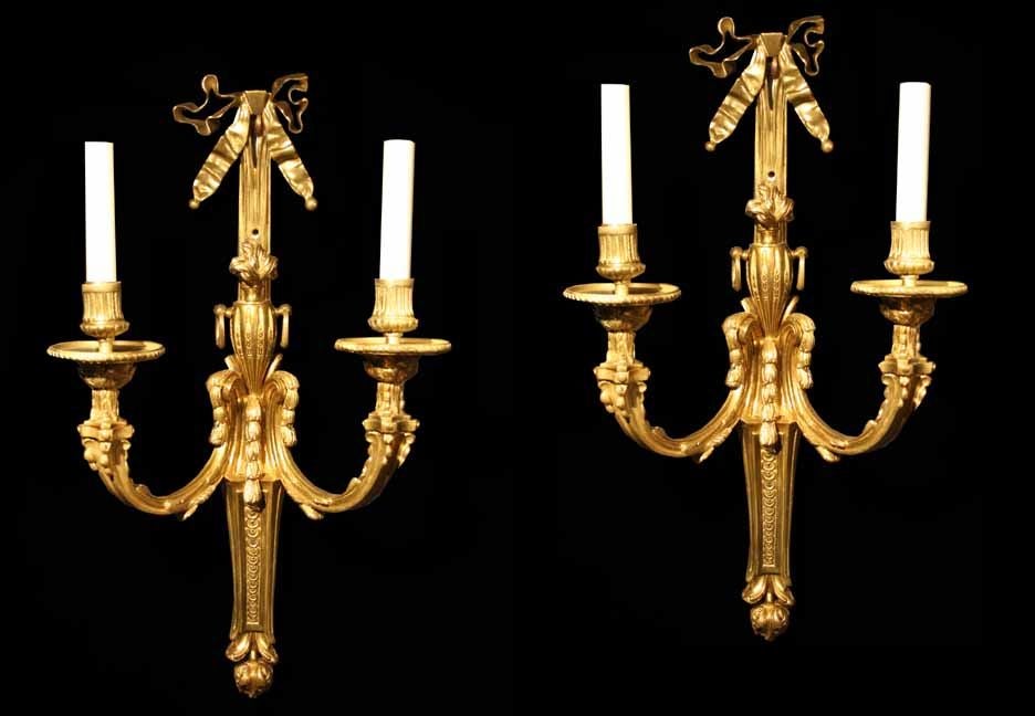 # S127 - Elegant PAIR fire gilt French Louis XVI  style sconces. These are well drawn with graceful lines and adorned with subtle neoclassical details. Each surmounted with a pretty tied bow above a neoclassical urn. The candles are held by fluted