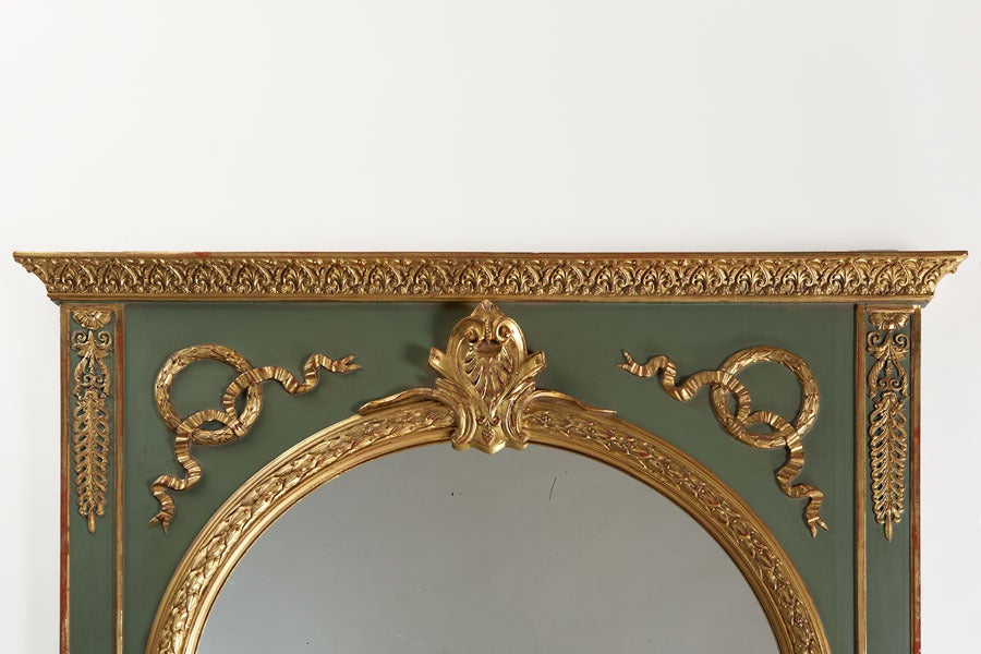 A large antique French Louis XVI style painted neoclassical style trumeau mirror from Belle Époque France circa 1895. The classical arch is highlighted with gold leaf and is framed with applied mouldings also highlighted with gold leaf. Framing the