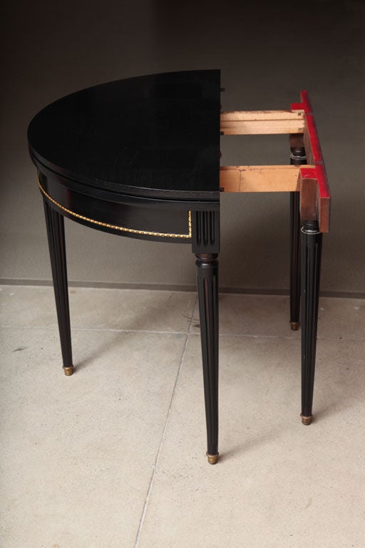 A black lacquered and brass-mounted fold-top demilune games/extending dining table (lacking leaves), attributed to Jansen.