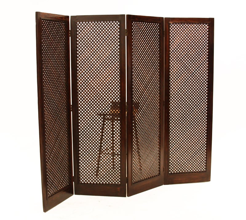 Tall four panel folding screen or room divider from Brazil. The latticed panels are hinged together with brass patinated hardware. The lattice work is made up of small rectangular wood strips allowing it to be a visually permeable room