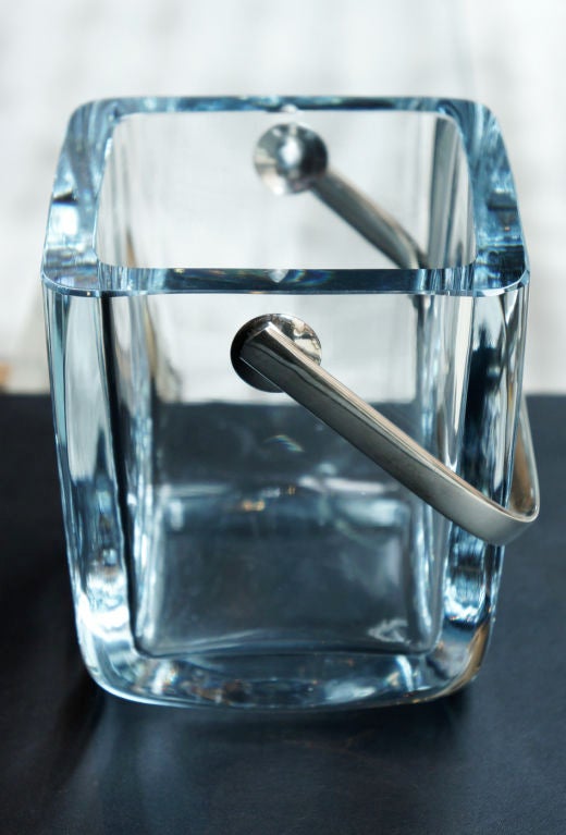 An exquisite Arctic-blue crystal ice bucket. The sterling silver handle is attached with perfectly designed pivots. Cartier's unparalleled attention to detail is evident in this rare item. Cartier signature on bottom.