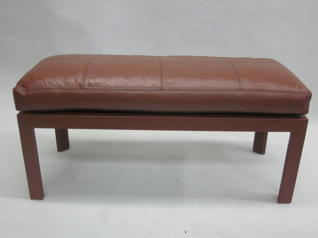 An elegant and sober French Mid-Century Modern style leather covered bench in the style of Jacques Adnet with a hand-sewn leather seat. The seat is stitched in a square pattern and sewn to the bench structure. 