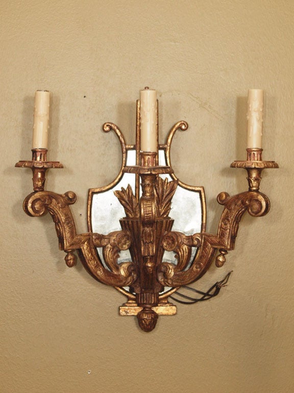 Handsome pair of French three-arm giltwood carved sconces with shield shaped mirrored back and quiver motif. The beeswax candle sleeves are perched on scrolling arms with acorn accents. Sconces are wired for USA.