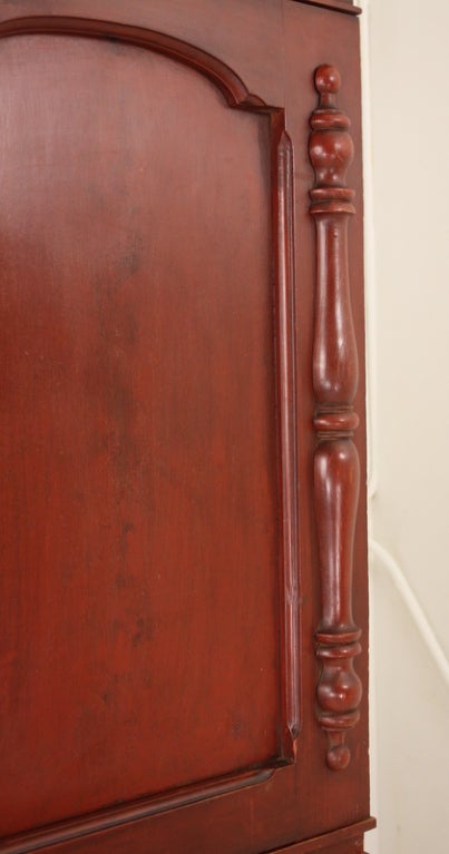 Antique pine Irish linen press with original deep-red paint. The cabinet doors with panels and hand-carved columns open up to two shelves for good storage. Below there are two smaller drawers above two larger ones. Note the horizontal faux grain on