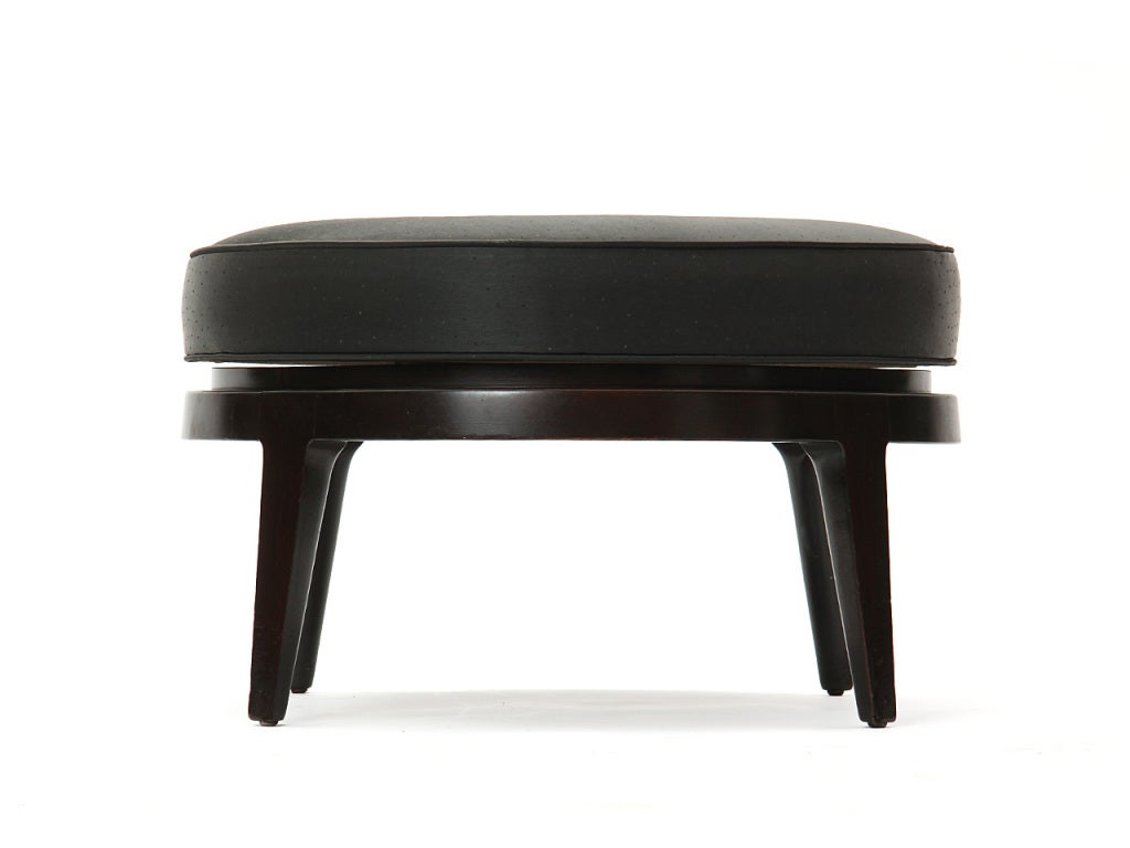 A circular swivel-seat ottoman with the original black, random-spot jacquard upholstery on a dark mahogany base with splayed, tapered legs.