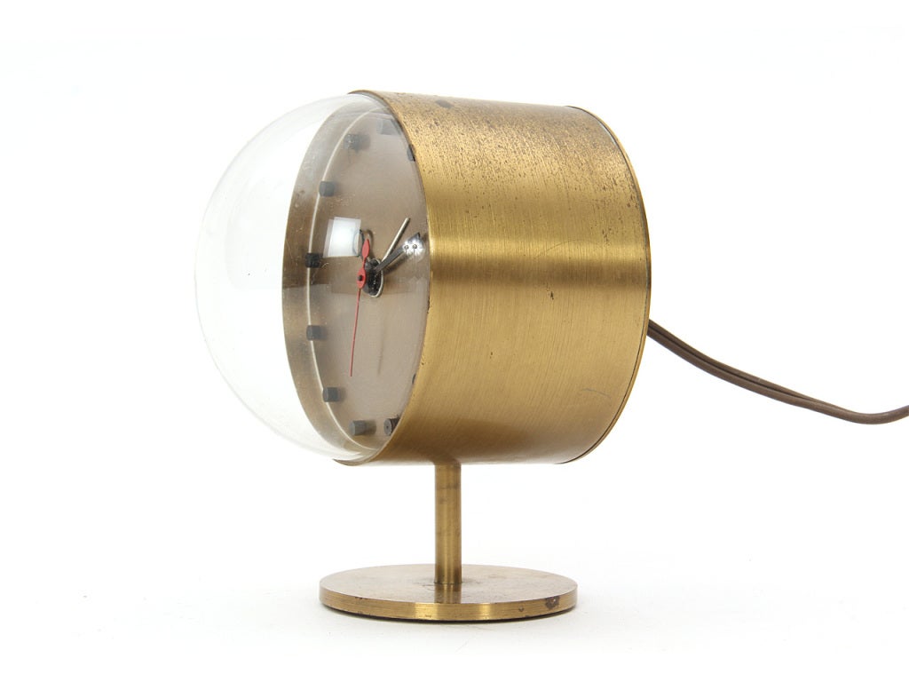 A petite electric table clock made from spun brass with a half-sphere glass dome resting on a simple brass base.