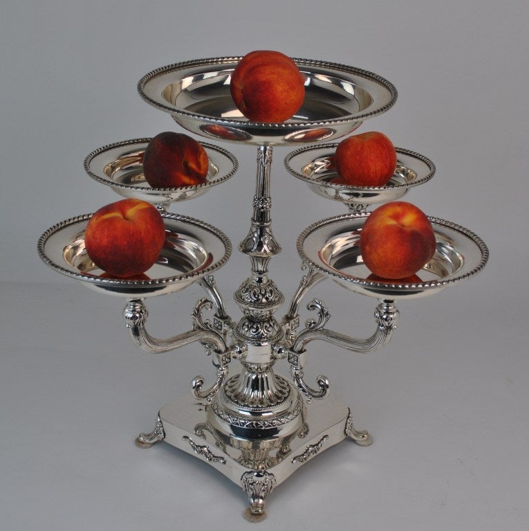 Regency-Style Epergne. Silverplated 5-basket epergne with unidentified logo on lower base, possibly a Sheffield mark. Etched and embossed decoration. Four scrolling support arms with silverplated baskets. Four scrolling feet.