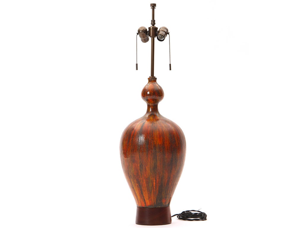 A bulbous ceramic table lamp with a slender neck on a teak base, with orange and brown brushed glazes.