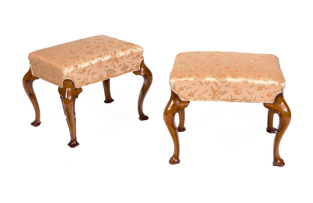 Pair of walnut stools with cabriole legs and trifid feet. With an exaggerated curve to the legs and the edges carved with C-scrolls.