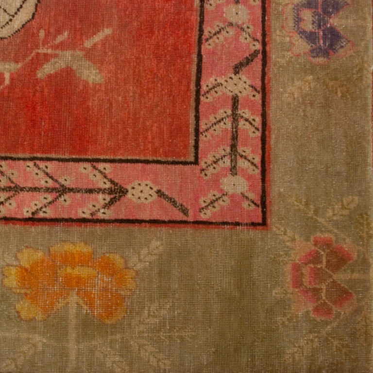 Tapis Khotan d'Asie centrale du début du 20e siècle avec des fruits et des fleurs sur un fond rouge entouré d'une bordure florale vert menthe.

Mesures : 8.9