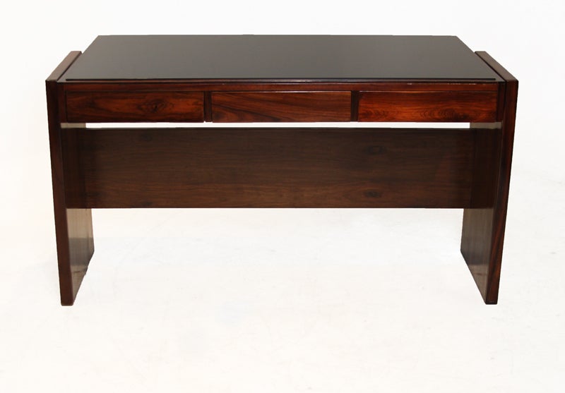 Rosewood desk designed by Brazil's Joaquim Tenreiro with a black reverse painted glass top and three drawers. This desk came from the Bloch, Editores headquarters, a building designed by Oscar Niemeyer and with interiors furnished by Sergio