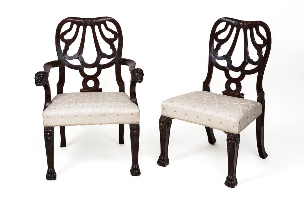 Set of 12 carved mahogany dining chairs, after Giles Grendey. Two armchairs and ten side chairs. With carved masks on the legs and armrests and paw feet.

Armchairs:
38" H, 27 1/2" W, 24 1/2" D.

Side chairs:
38" H,