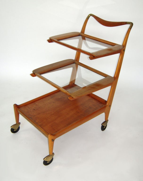 Superb example of Italian mid-century design. Trolley/tea/bar cart designed by Cesare Lacca. Two removable graduating tray shelves, and a stationary wood bottom. Brass capped rollers, and brass details also on the curvaceous handle. Seen in Don