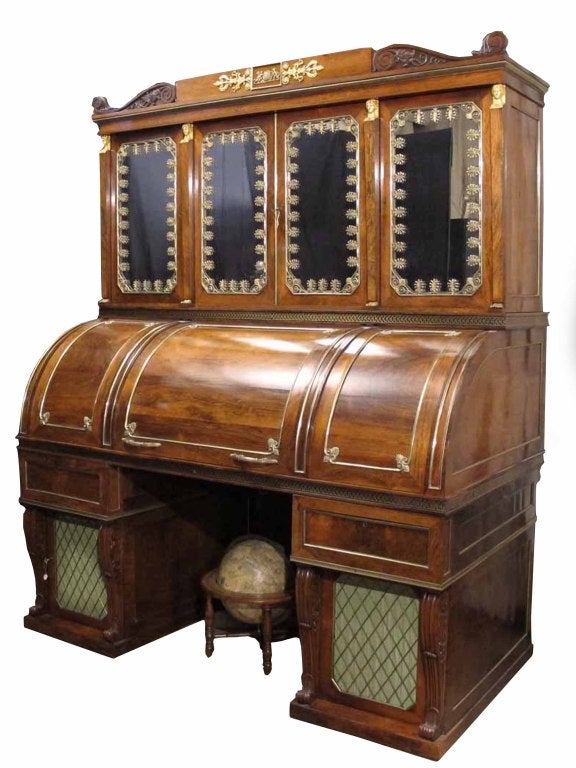 # D274 - Important Regency rosewood cylinder desk in the neoclassical taste with distinctive gilt bronze mounts. The flat plinth cornice flanked by carved corbels and centering bronze mounts of putti holding a globe. The upper section with four
