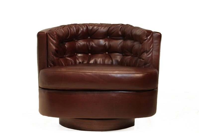 Pair of tufted barrel swivel chairs upholstered in a dark burgundy  leather. The chairs sit on a round Rosewood base. By Milo Baughman.
Seat depth measures 22