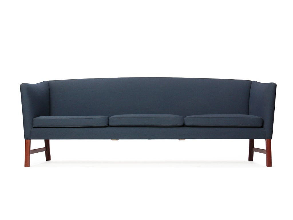 A sofa with a raised, tight back and sloping arms, retaining the original upholstery, on Cuban mahogany legs.