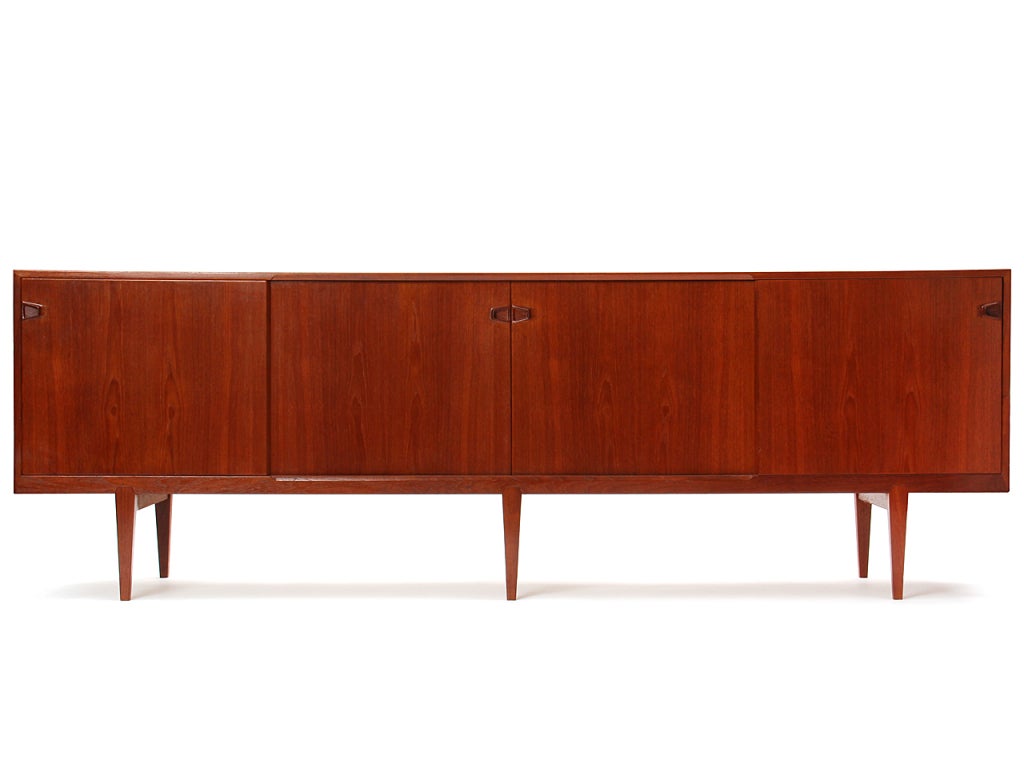 A teak credenza with four sliding doors concealing shelving and drawers over six tapered legs.