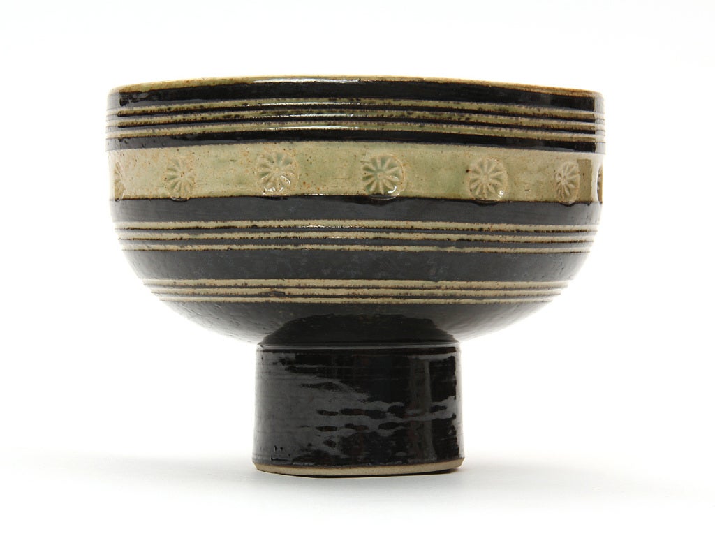 A ceramic bowl with tan and black bands of glaze and a repeating star burst pattern.