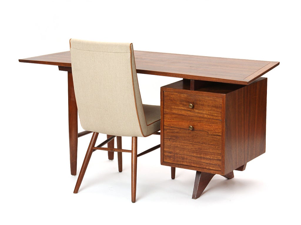 A walnut two (2) drawer desk with an overhanging, concave-front top and brass pulls and dowel legs. By George Nakashima for Widdicomb.