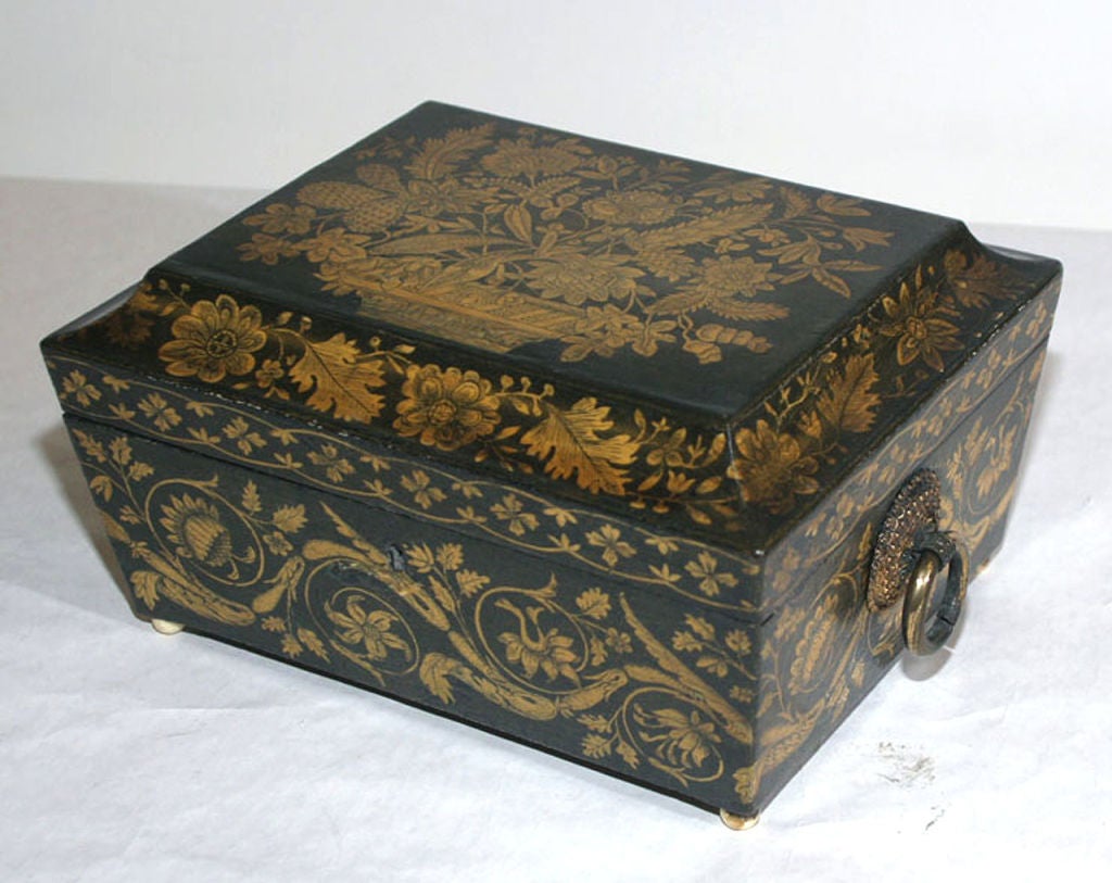 OF TAPERED RECTANGULAR FORM, THE DOWNSWEPT LID DECORATED WITH AN ARRANGEMENT OF FLOWERS AND LEAVES IN A BASKET, ALL FOUR SIDES DECORATED WITH LEAFY SCROLLS AND FLORAL MOTIFS, FITTED WITH RING HANDLES AND BALL FEET, THE INTERIOR WITH A
