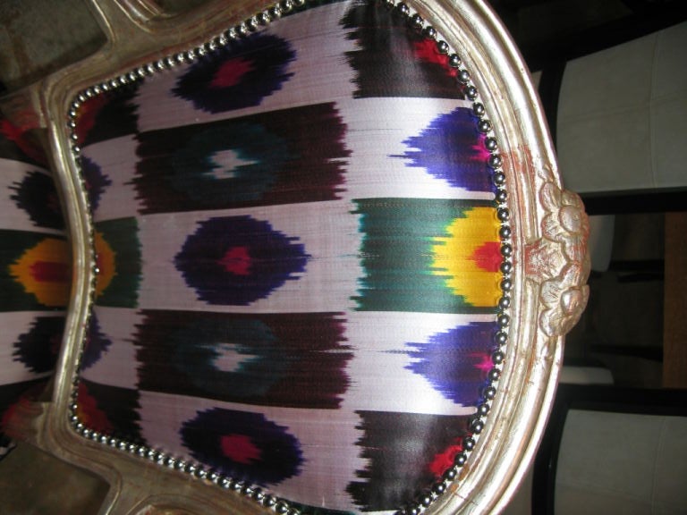 Beautiful 22k water gilt finish in white gold. Hand-carved floral motif. Reupholstered in a vibrant ikat and velvet back.