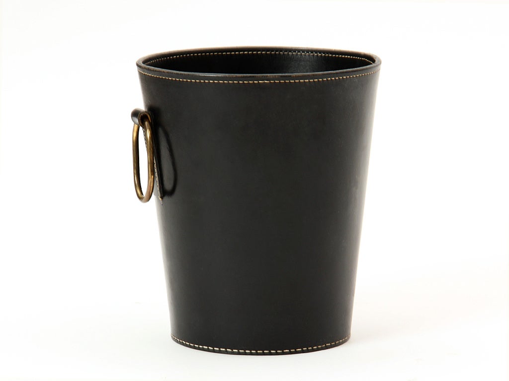 A hand-stitched black leather wastebasket with an oval brass handle.
Brown also available.