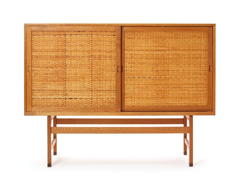 An oak two door high cabinet with woven cane doors on an open base with rosewood capped feet.