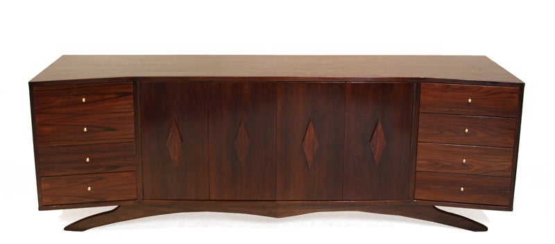 Massive walnut case credenza with with diamond-shaped Rosewood pulls, Rosewood drawers, polished brass pulls, and and elegant solid Walnut sculptural base. The end compartments with drawers flare out from the body slightly. The interior dimensions