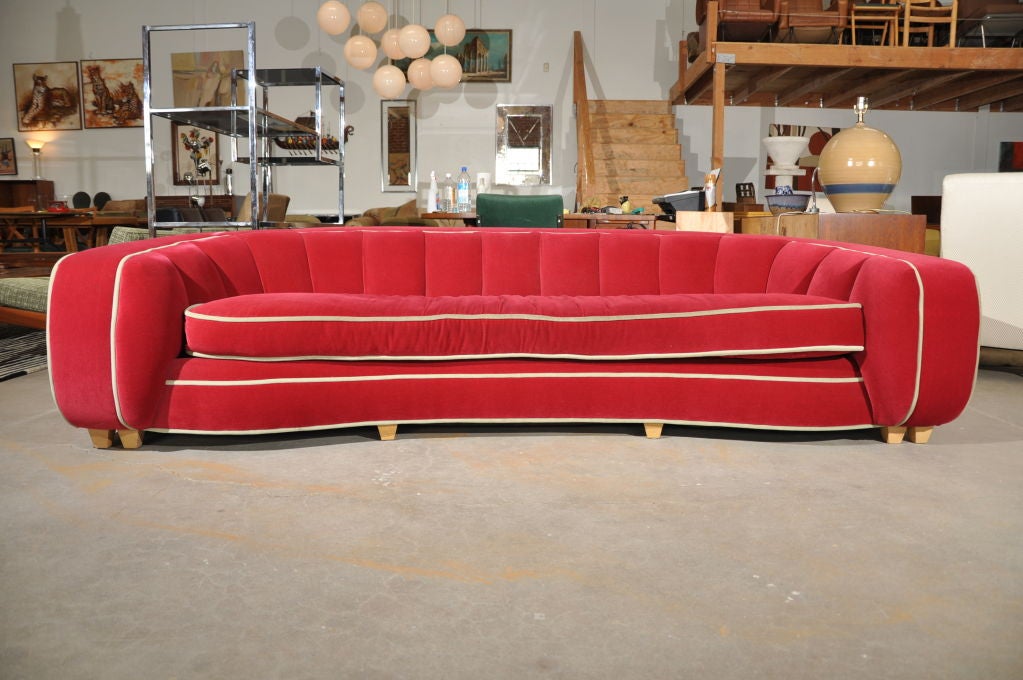 Luxurious, large and comfortable, made of red velvet with grey piping, this plush sitting area is set upon a wooden frame with nine legs supporting it.