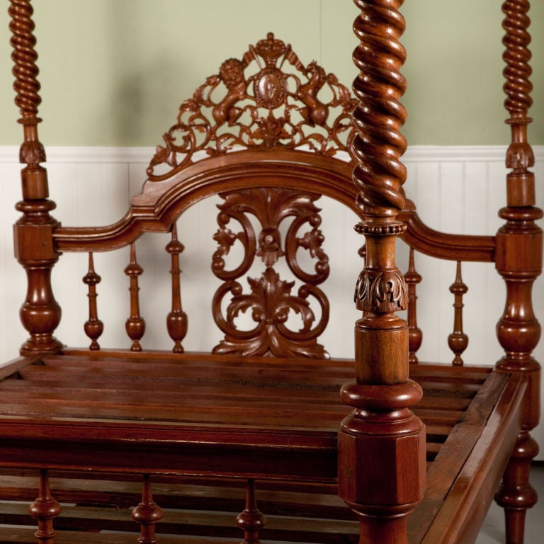 Anglo-Indian four poster bed with canopy in carved teak. Spiral turned posts, spindle headboard and foot board between carved rails and elaborately carved head board. Coat of arms carved on head board. Fits queen size mattress.