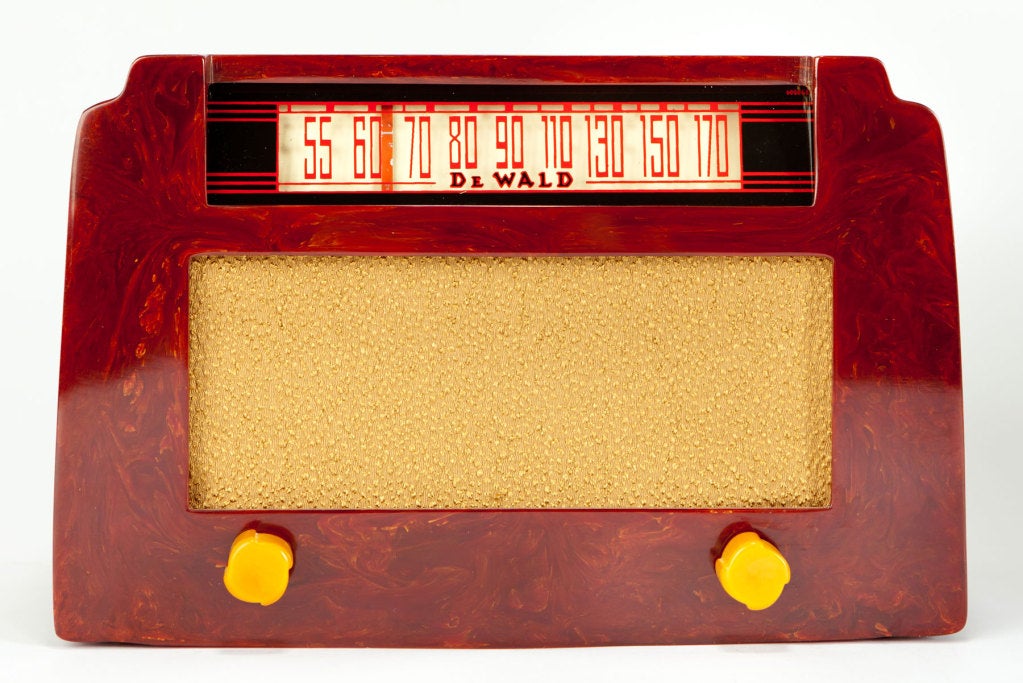 This clean American art deco Catalin radio known to collectors as the “step top” was made by DeWald Radio Manufacturing, Long Island, New York ca 1946. The radio, in cherry red with yellow swirls and yellow knobs, is in excellent condition save for