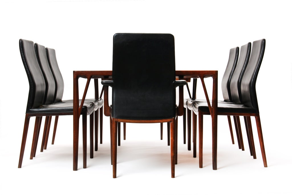 A rare and beautiful dining suite in rich Brazilian rosewood, the table, which can be extended with two leaves, having expressive braces which support carved dowel legs.  The sculptural rosewood dining chairs retain their original black leather;