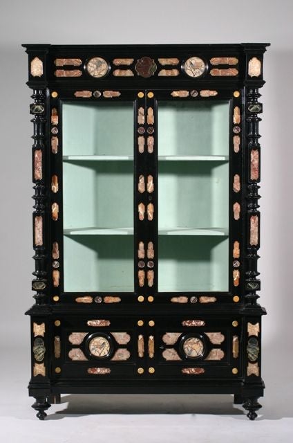 An Italian Third Quarter 19th Century Baroque Style Marble Inset and Pietra Dura Inlaid Ebonised Cabinet; the moulded top above a fretwork carved case with marble and glass on the front and both sides, above two cabinet doors decorated with four