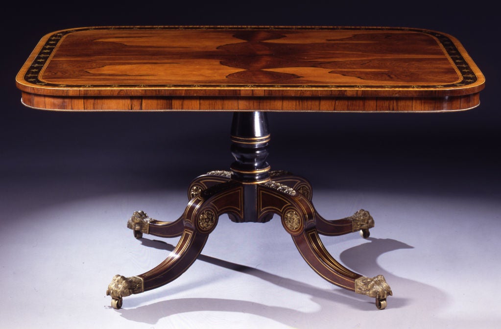The top with finely matched veneers with a calamander border inlaid with brass stars and flowers; the parcel-gilt, ebonised pedestal issuing gilt-brass mounted downswept legs with brass stringing.