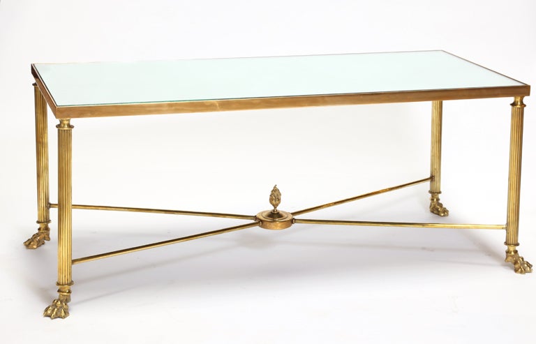 French brass cocktail table with lion paw feet with x-base stretcher and neoclassic flame finial. Inset antique glass mirror top.