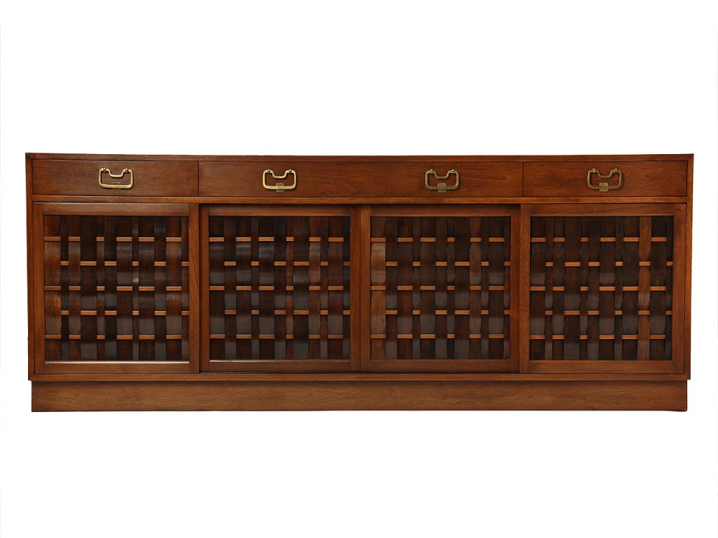 A rare woven front credenza with walnut strips interlacing unique rectangular rods. Four (4) drawers with brass pulls over four sliding doors with interior drawers and shelves.