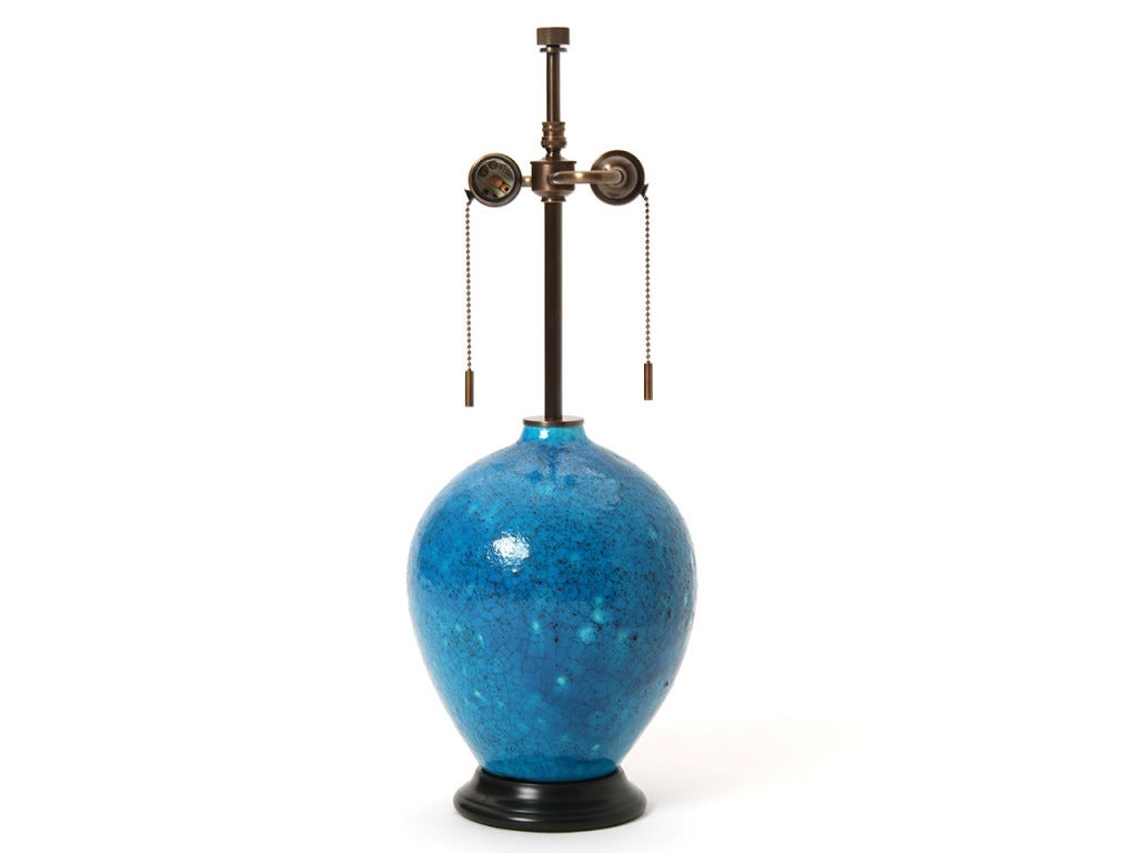 A petite blue ceramic lamp with a crackle glaze on a black pedestal base.