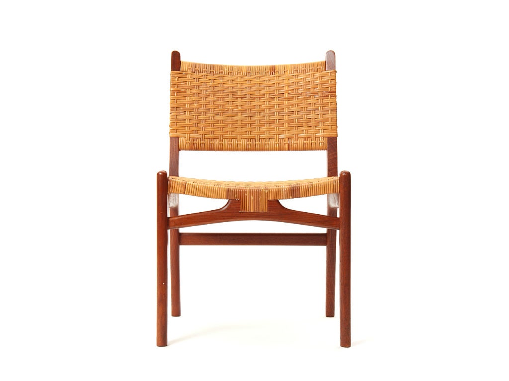 A fine and architectural dining chair having an exposed carved frame in rich teak with woven cane upholstery.