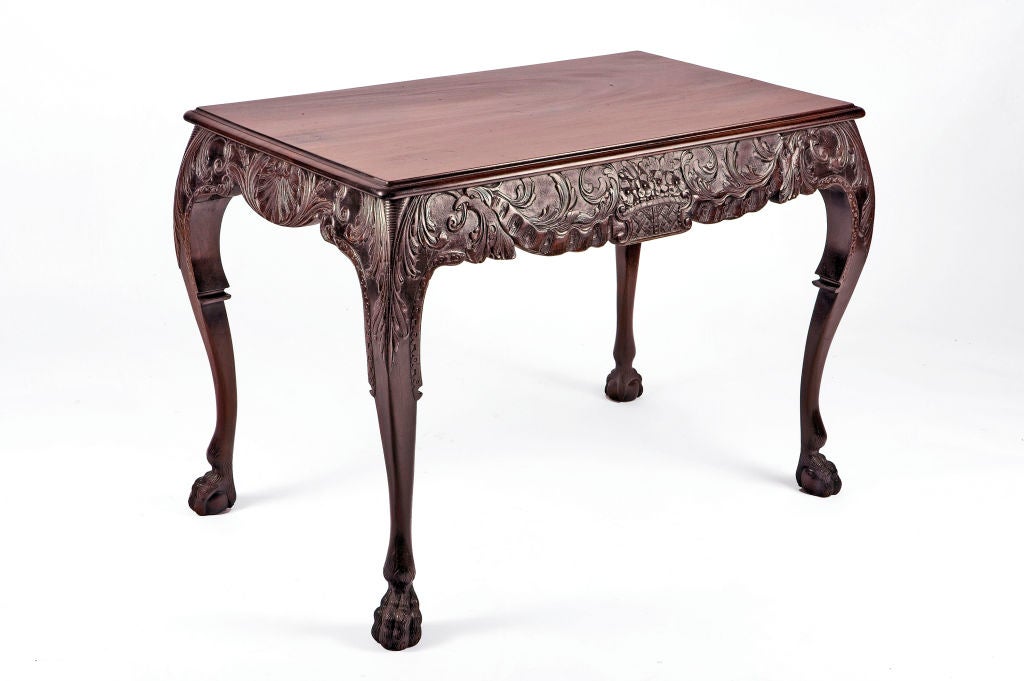 Mahogany center table. With a foliate carved frieze centered by a basket of flowers, on carved cabriole legs ending in hairy paw feet.