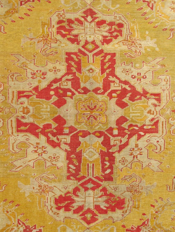 This gorgeous antique Oushak carpet holds a magnificent and commanding medallion composed of multifaceted sub-geometric designs. Four complimentary cornices elegantly mirror the medallion's esthetic in a refined manner. The entire field is