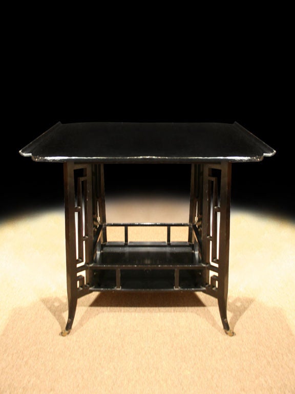 Anglo-Japanese ebonized 'Pagoda' table, the rectangular top having shaped corners and curl-up edges above fretted leg supports connected by a pierced undertier and raised on splayed feet with brass casters. 
Japanese art and objects were a rich