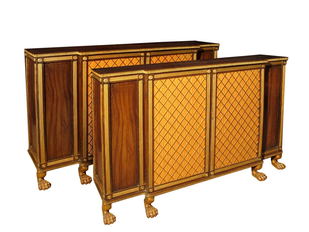 Elegant PAIR Regency rosewood breakfront side cabinets enriched with gilt decoration. The pair of central  grillwork doors flanked by a pair of wood panelled doors all framed by brass molding and details. Raised on short carved and gilt paw