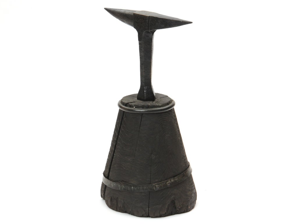 A wrought iron anvil with an ebonized wood base.