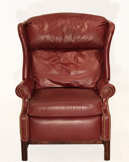 Wingback leather recliner in original Burgundy leather with brass nailheads along the front of the piece. The four Mahogany finished legs are connected by a stretcher. The piece can be partially reclined as well as fully. Dimensions of the fully