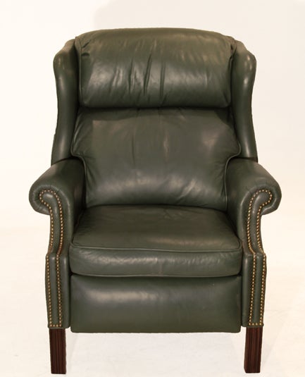 A wingback Chippendale leather recliner in a sage green leather with brass nail heads adorning the front. The chair features four carved straight leg Mahogany finished feet. The chair can be partially reclined or fully. The dimensions of the chair