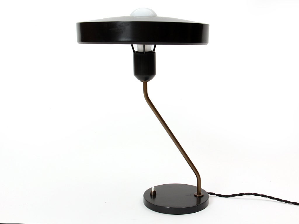 A desk lamp consisting of two black metal discs offset and connected by a bent brass tubular support.